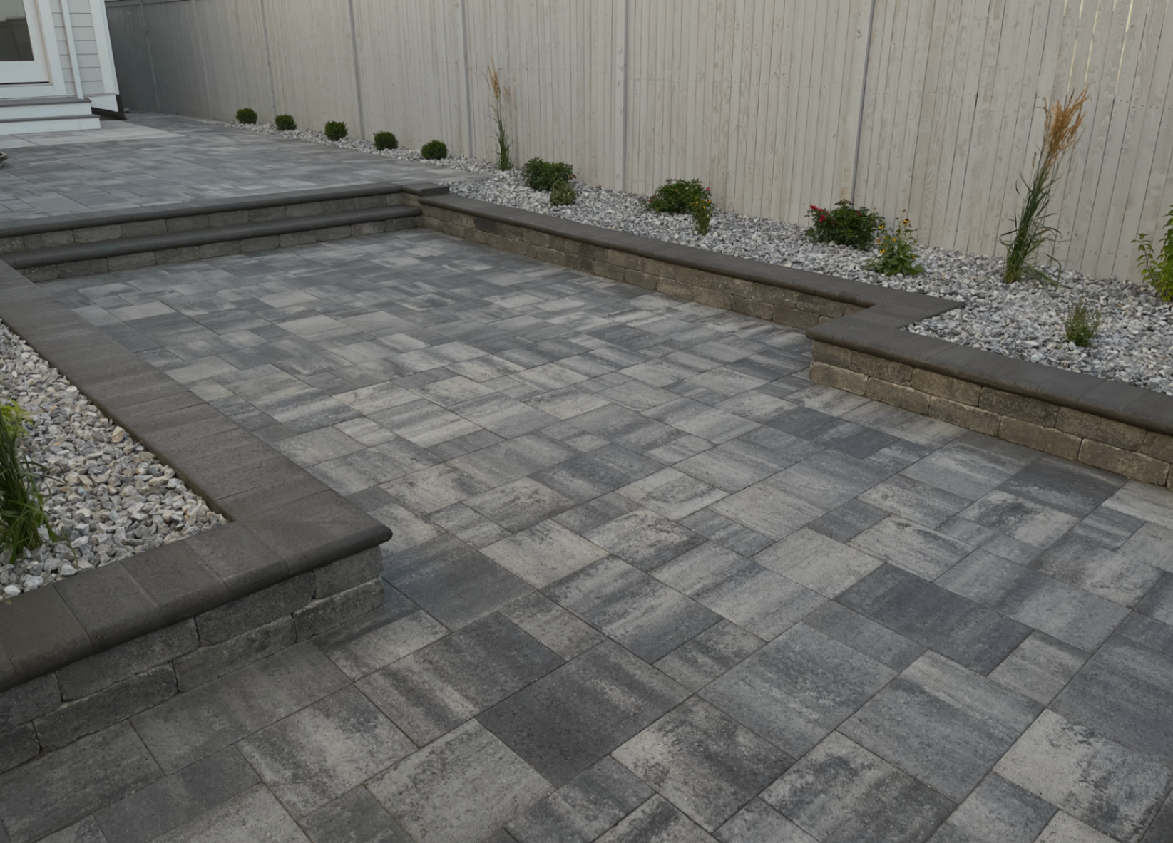 Finished gray paver patio with steps, seating walls, and decorative rock borders