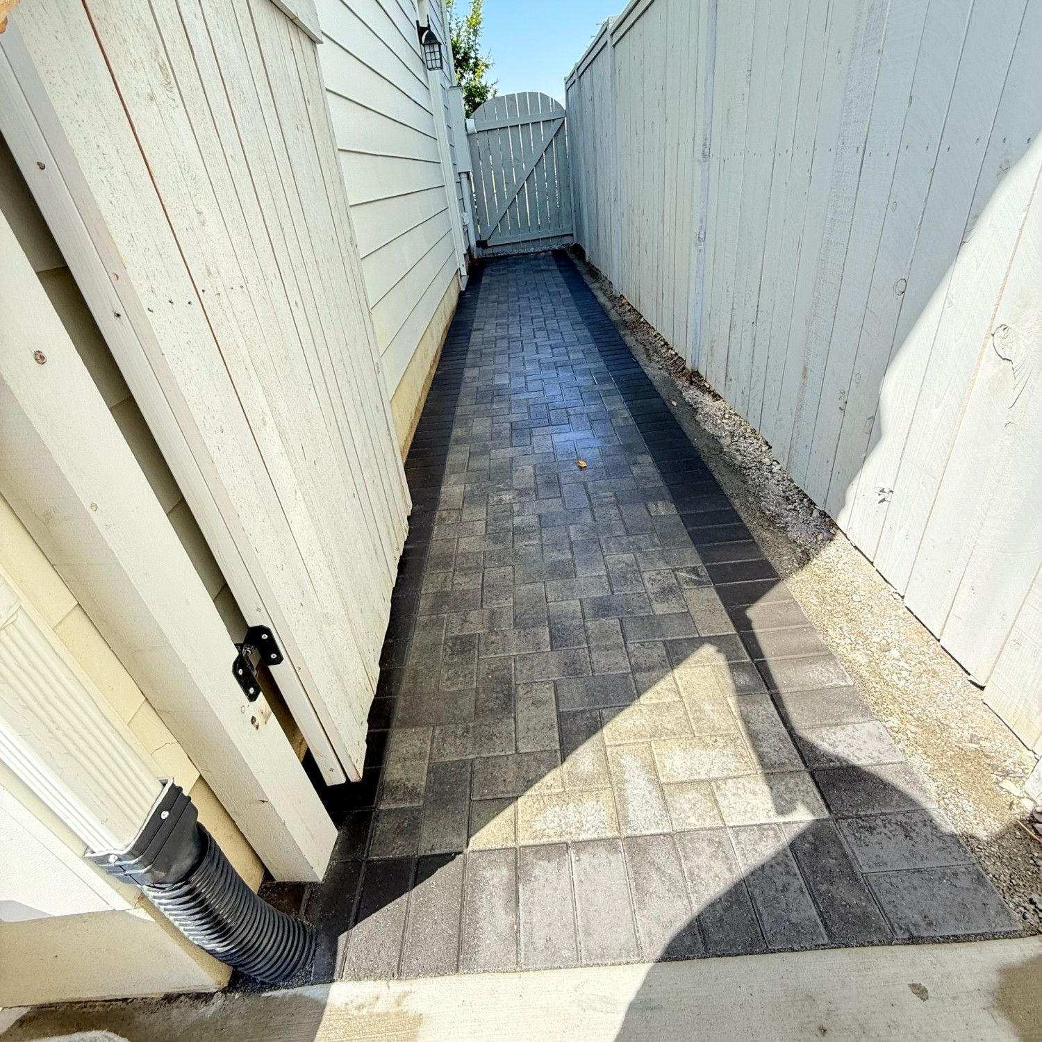 Narrow paver walkway between house and fence leading to a wooden gate