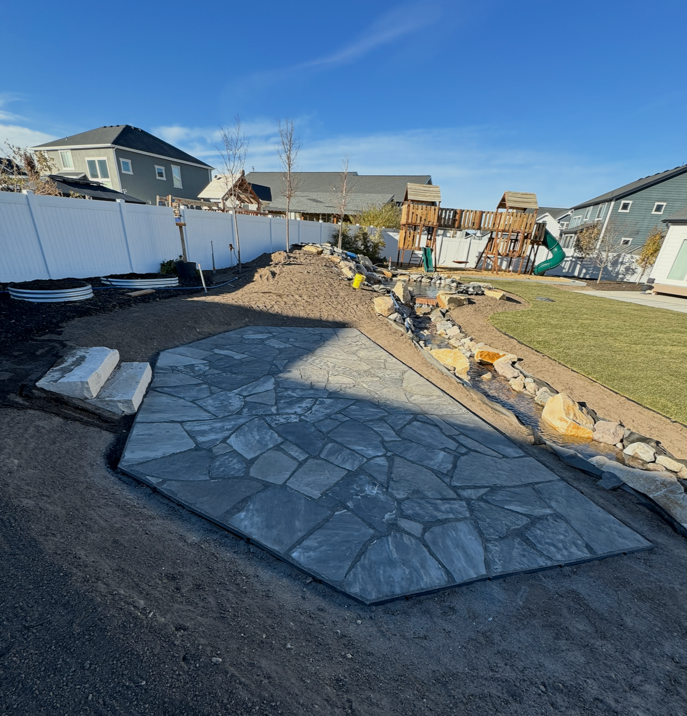 Large flagstone patio installation in progress beside lawn and water feature