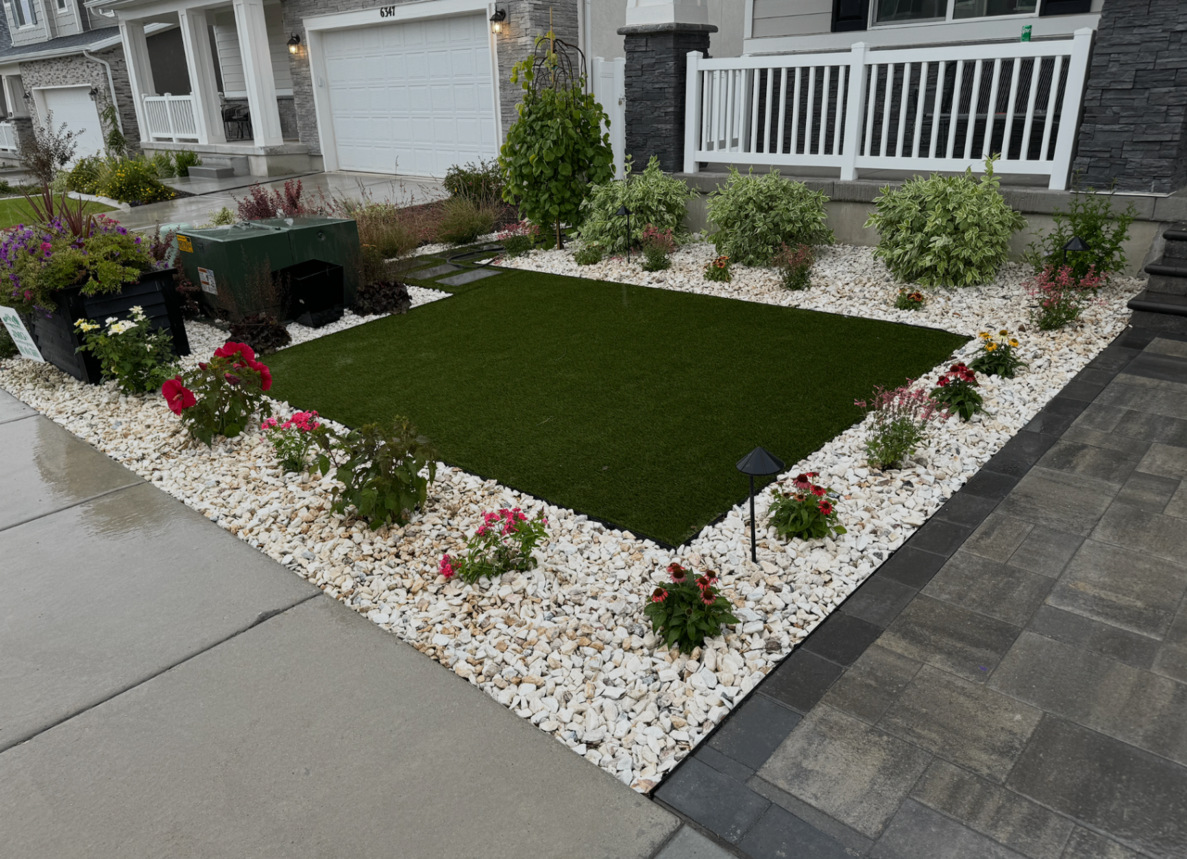 Front yard landscaping with green lawn, white rock beds, flowers, and paved edging